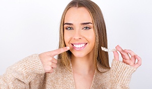 a woman holding clear aligners and pointing at her teeth